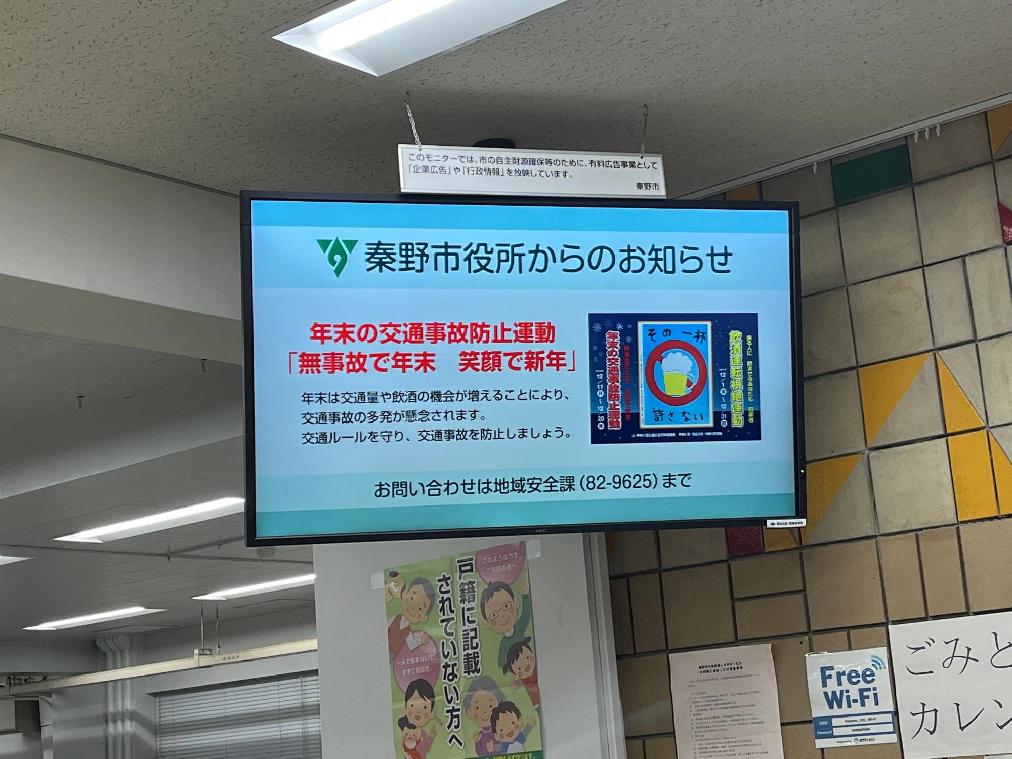デジタルサイネージに「秦野市役所からのお知らせ」が表示されており、「年末の交通事故防止運動」について呼びかける注意喚起を促す画像が掲載された写真