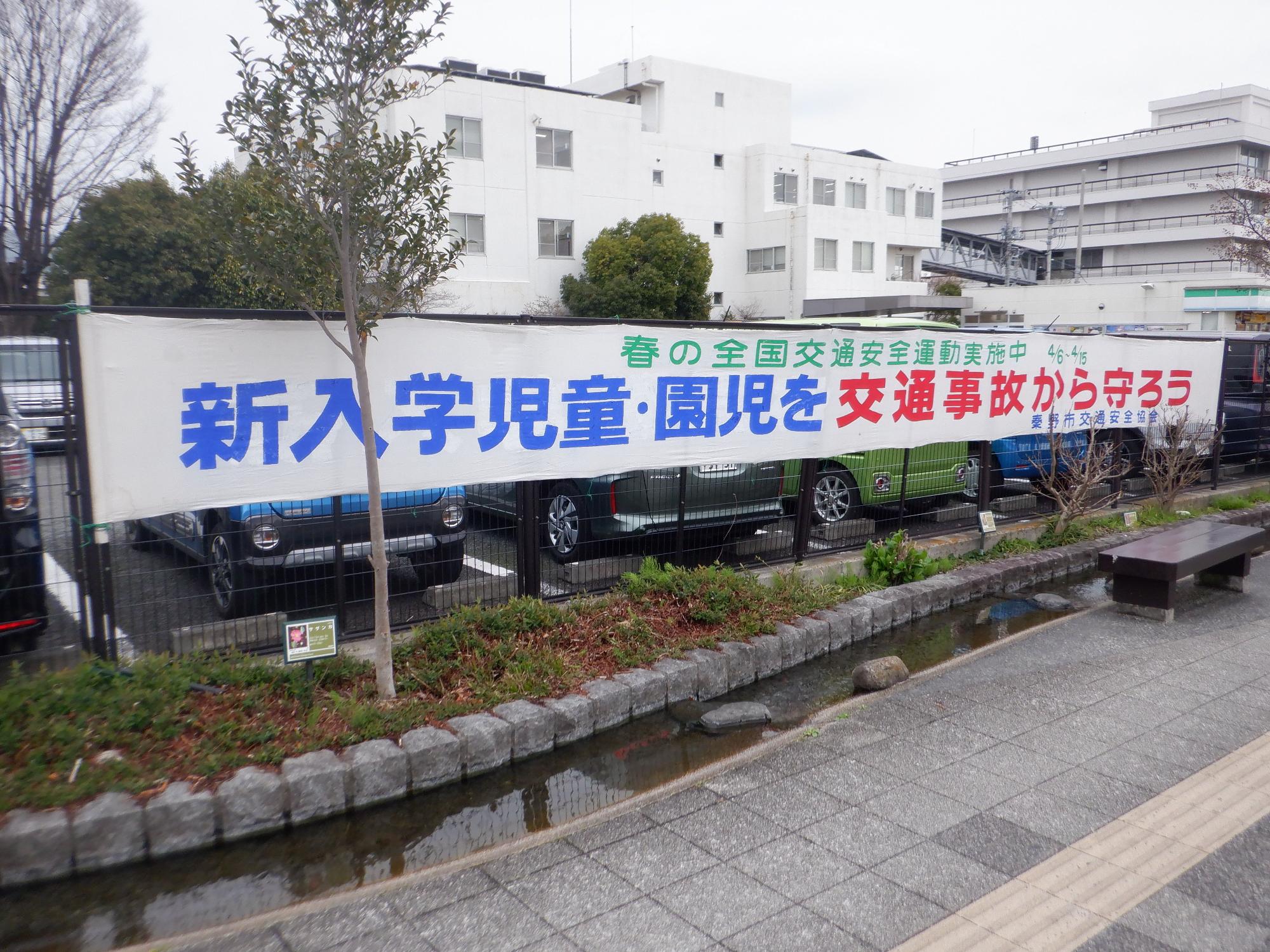 「新入学児童・園児を交通事故から守ろう」と書かれた横断幕が駐車場のフェンスに掲げられている写真