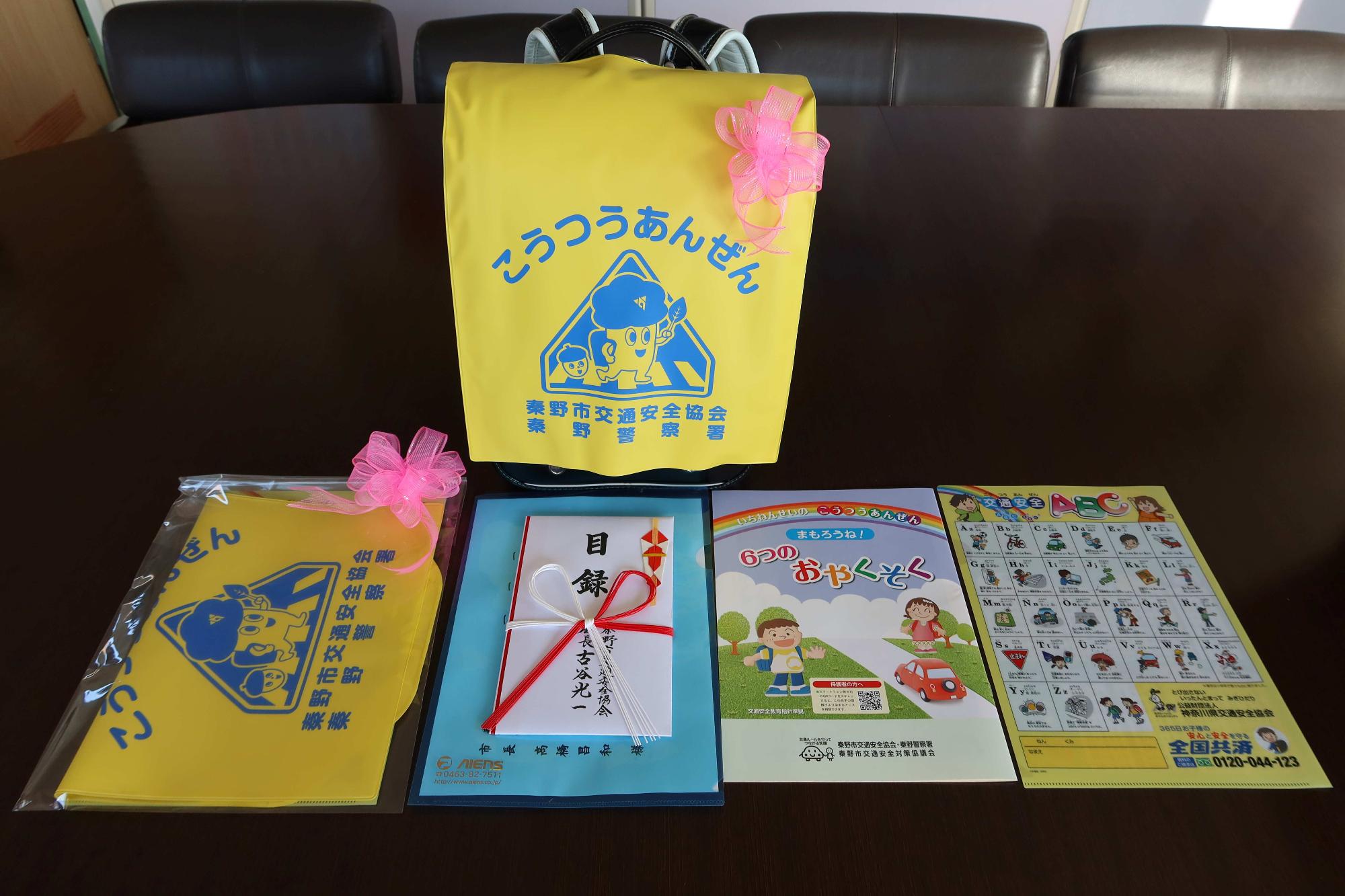 「こうつうあんぜん」と書かれた黄色いランドセルカバーを中心に、新一年生向けの啓発グッズ一式がテーブルの上に綺麗に並べられている写真