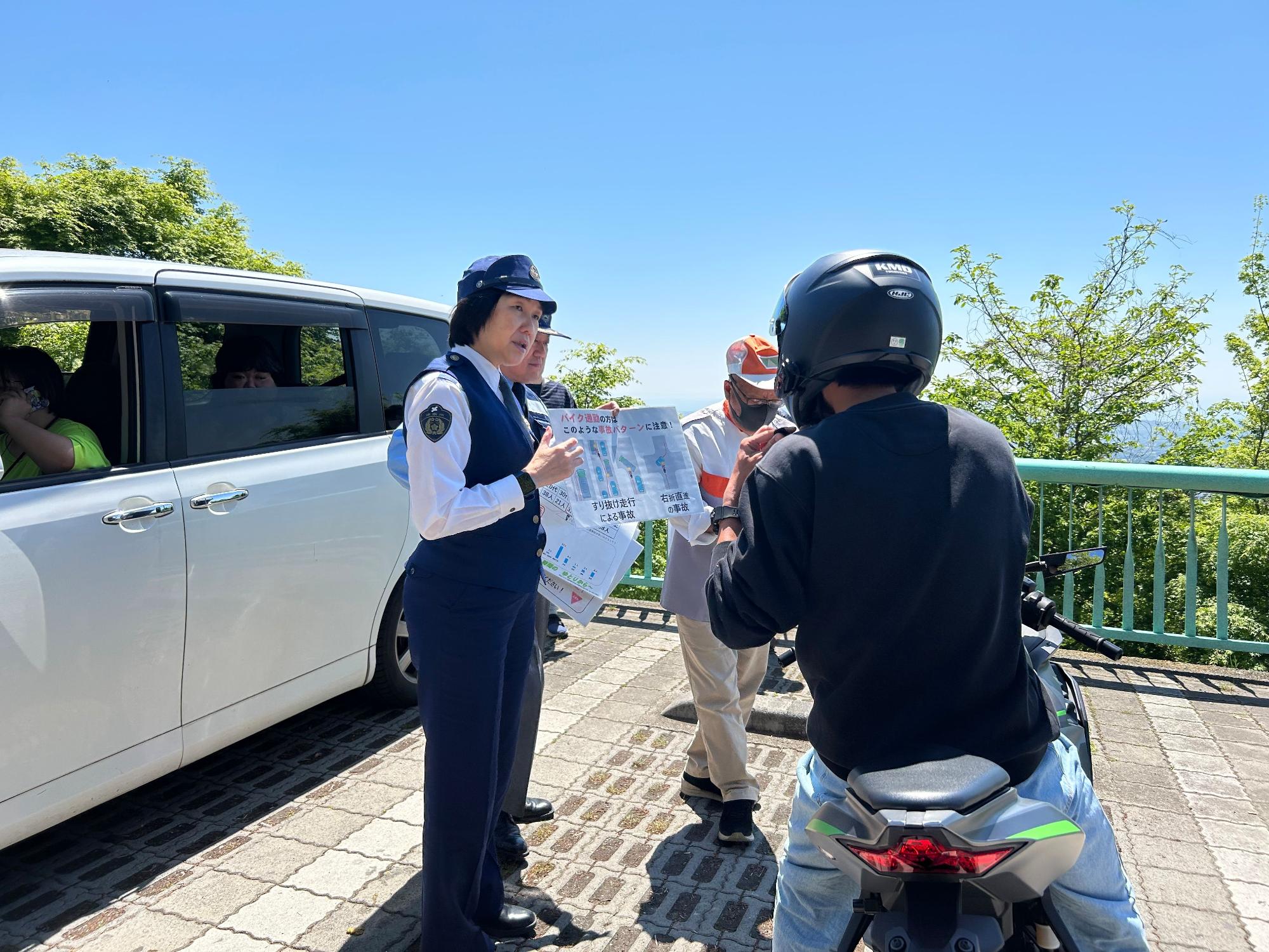 女性警察官がチラシを差し出しながら、オートバイに乗ったライダーに交通安全の呼びかけをしている写真