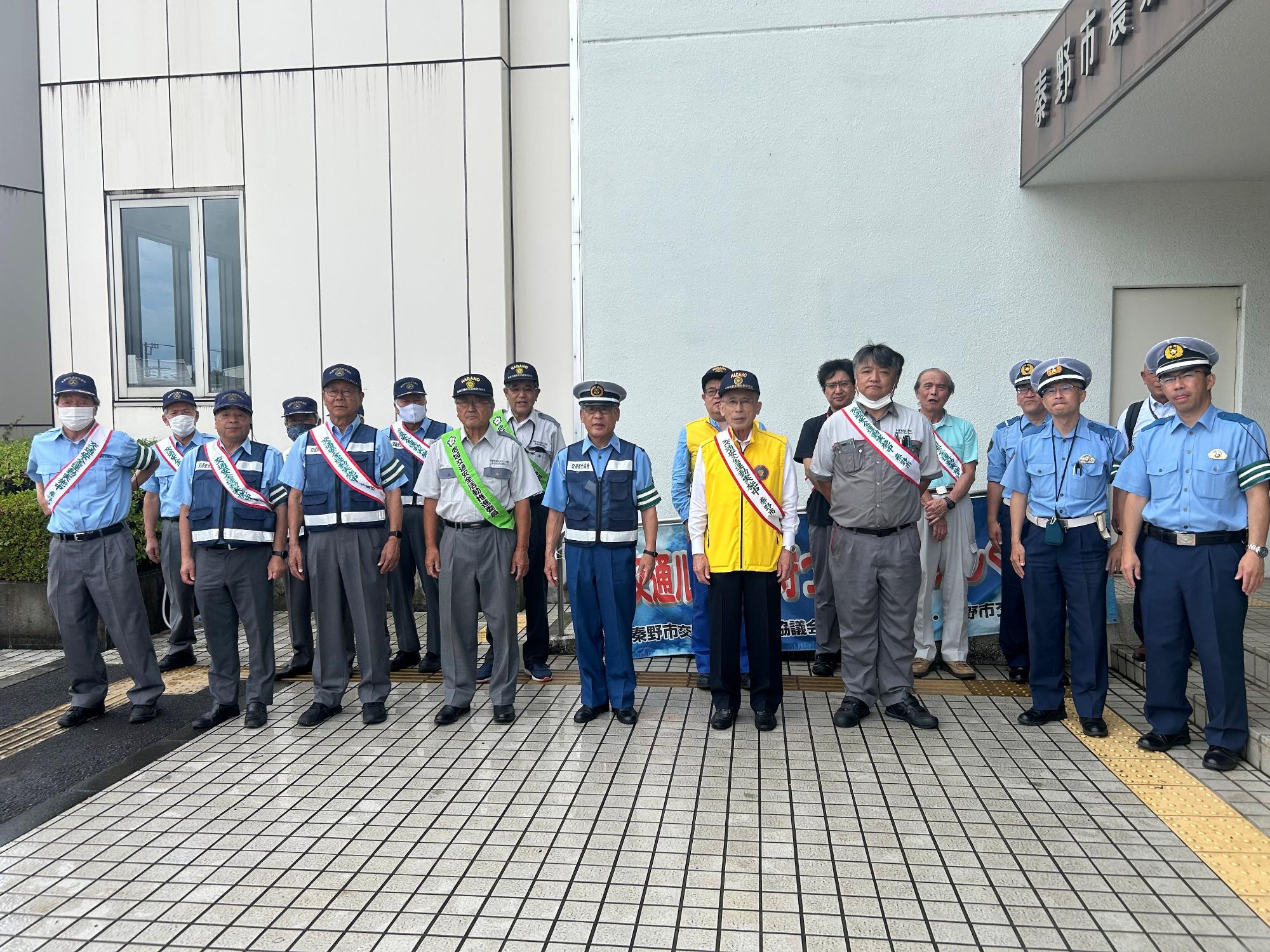 警察官や交通安全のたすきをかけた市民ボランティアなどが一列に並んで立っており、交通安全運動の集合写真