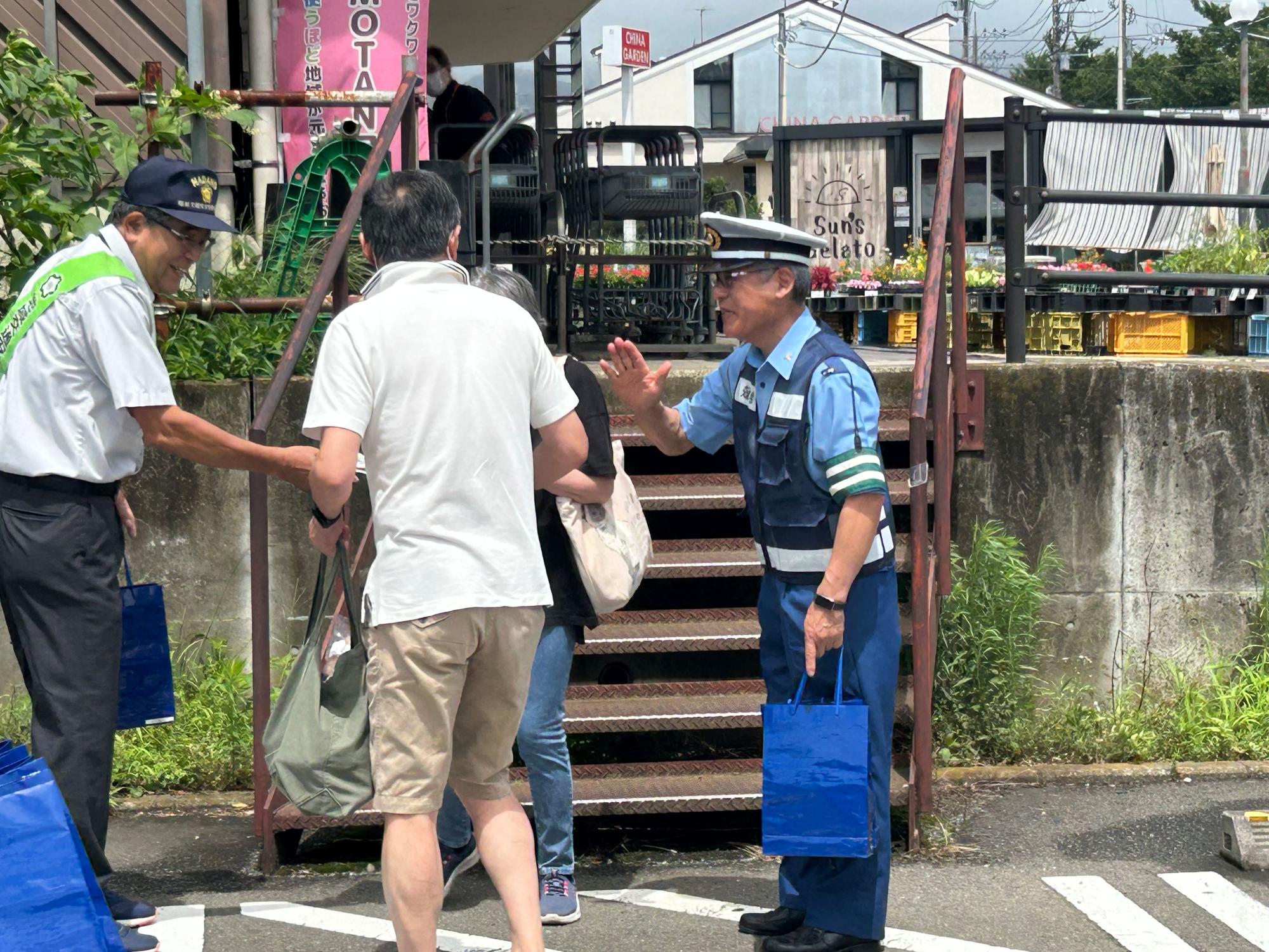 青い制服に安全ベストを着用した警察官が、すきをかけたボランティアの方と一緒に市民へ交通安全運動を行っている様子の写真