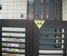 横長の格子状の門扉の中央に「防犯」の文字が赤で書かれたた逆三角の黄色いステッカーが貼付されている写真