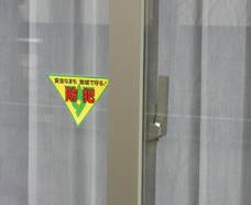 「防犯」の文字が赤で書かれたた逆三角の黄色いステッカーが窓ガラスに貼られている写真