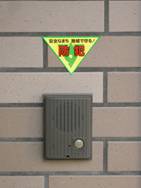 レンガ調の外壁に設置されたインターホンの上部に「防犯」の文字が赤で書かれたた逆三角の黄色いステッカーが貼付されている写真