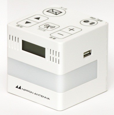 白とグレーの日本アンテナ製の立方体型のデジタルラジオで、上部には電源やラジオ、音量調節、メールなどの操作ボタンと小さな液晶画面があり、側面にはUSBポートとスピーカーのグリルが配置されている専用端末写真