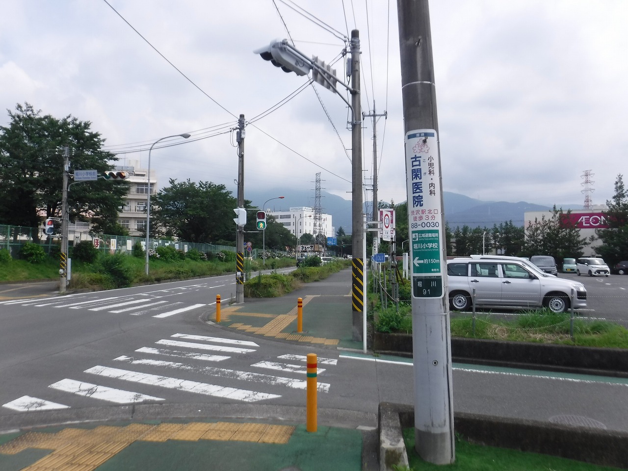 手前に白線と点字ブロックが施された横断歩道がある角に立っている1本の電柱に広告が設置されている写真