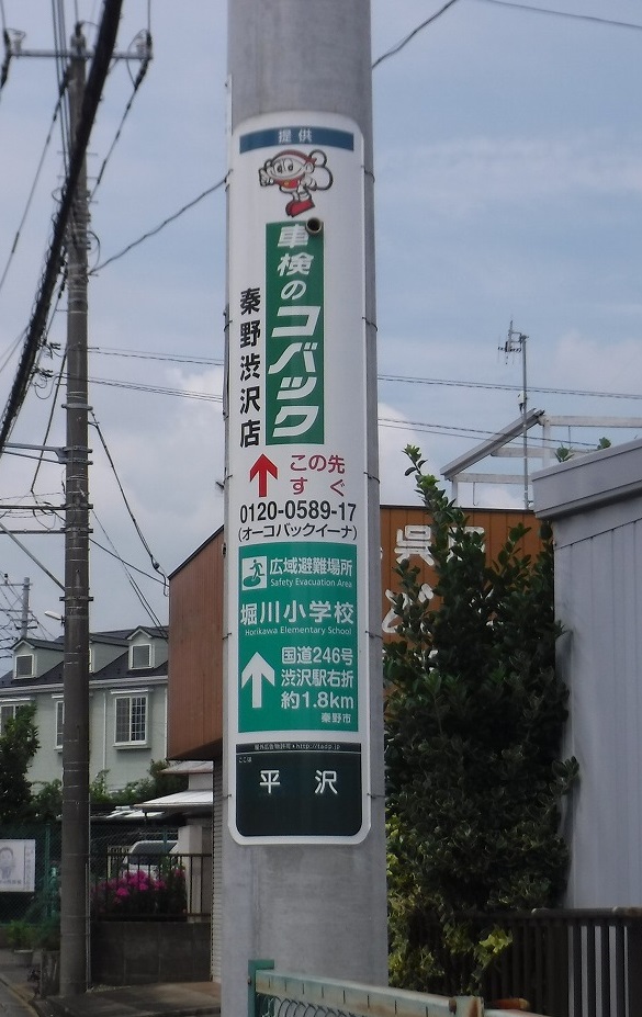 公道に立つ電柱に設置された縦長の「北村自動車整備工場」案内表示板の写真
