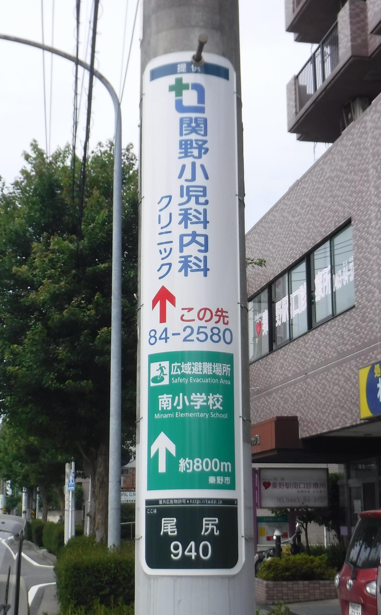 公道に立つ電柱に設置された縦長の「関野小児科内科クリニック」案内表示板の写真