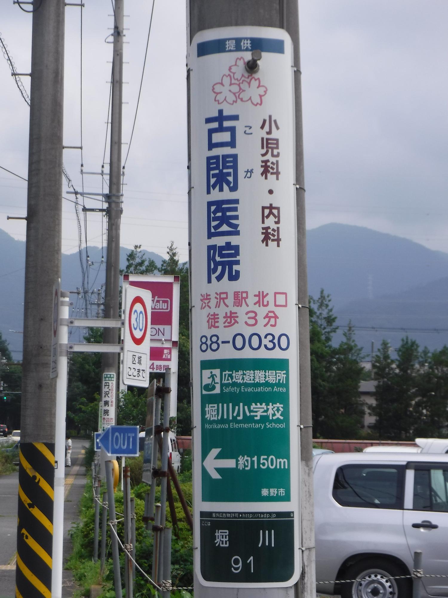 公道に立つ電柱に設置された縦長の「古閑医院」案内表示板の写真