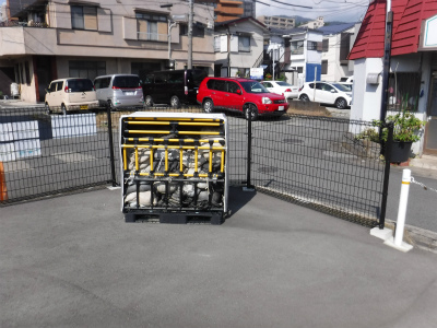 住宅街の駐車場に設置された金属製メッシュフェンス付き防災倉庫の内部に土のうが格納されている写真