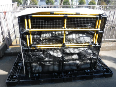 屋外に設置された黒いメッシュパネルと黄色いフレームで構成された折りたたみ式防災倉庫の中にたくさんの土のうが準備されている写真