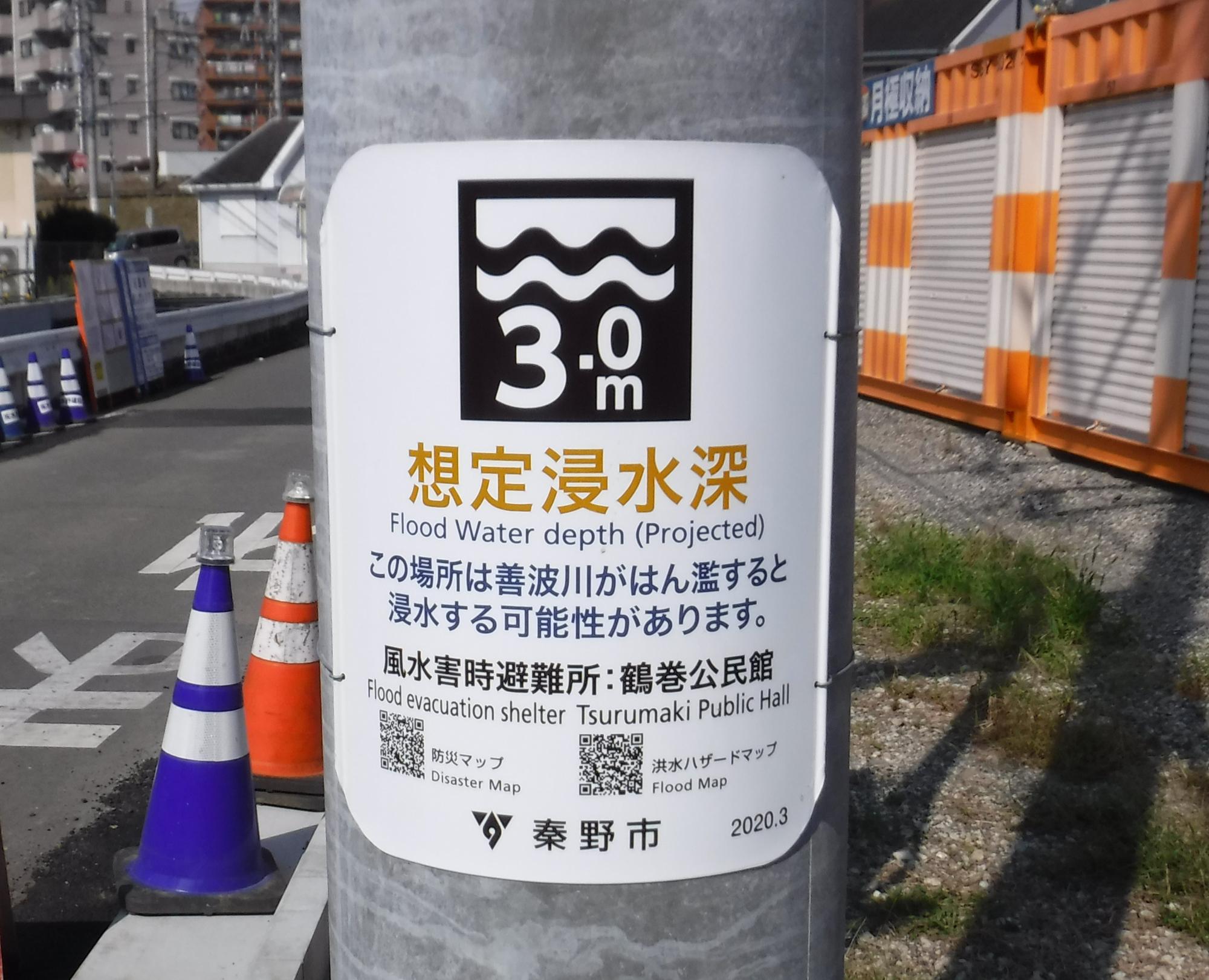 電柱に貼られた秦野市が発行した洪水ハザード表示板の写真で、鶴巻川が氾濫した際のこの場所の「想定浸水深」が「3.0メートル」であることと、風水害時避難場所が「鶴巻公民館」であることを示した電柱看板の写真