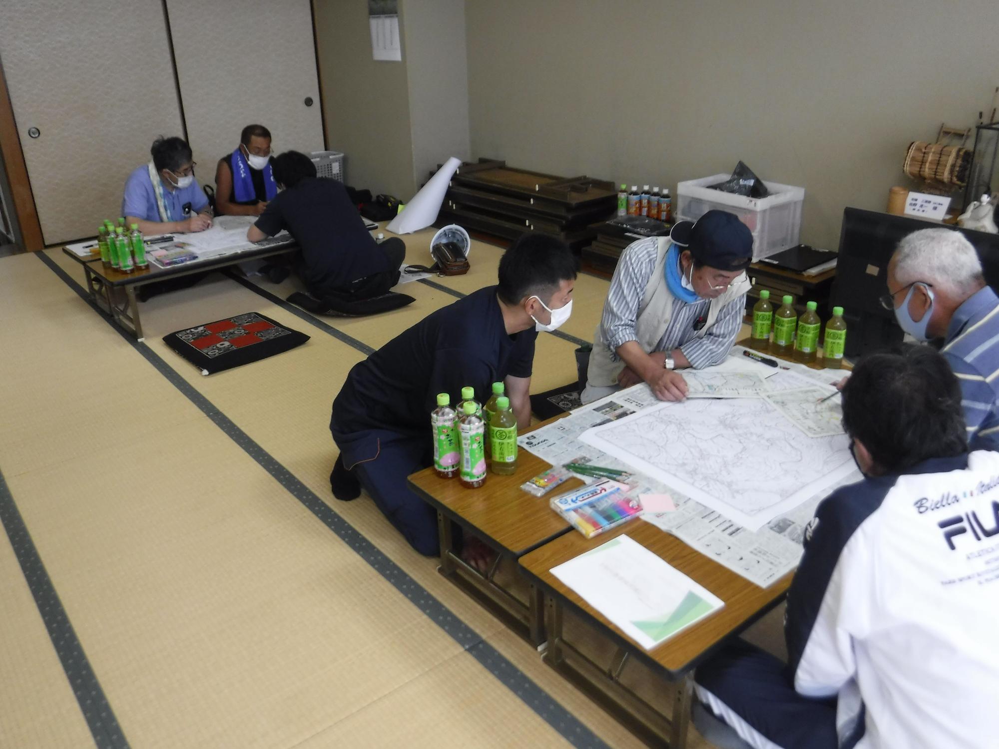 和室でマスクを着用した数名の男性が、畳の上に置かれた座卓を囲み、地図のような大きな紙を広げて、防災マップや防災計画に関する話し合いを行っている写真