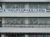 公共施設の白い外壁とガラス窓の間に「女性に対する暴力をなくす運動11月12日~11月25日」と紫リボンマークを配した白地の横断幕が掲げられた女性支援啓発キャンペーンの建物外観写真