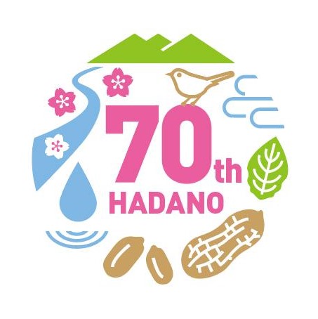 丹沢連峰、川、桜の花、市鳥のうぐいす、たばこの葉、落花生などのイラストが円形に囲まれ、中央にピンク色で「70th HADANO」の文字が配置された、市の70周年を祝うロゴマークのイラスト