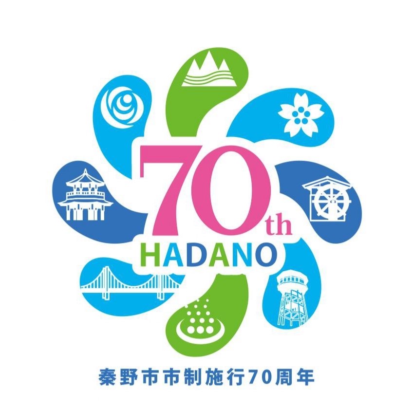 「秦野市市制施行70周年」という文字が青色で下部に配置され、カラフルな8枚の花びらのような図形の中に、温泉や山のマークなど秦野市の名所が描かれ、中央に「70th HADANO」の文字が配置された、市制施行70周年を記念するロゴマークのイラスト
