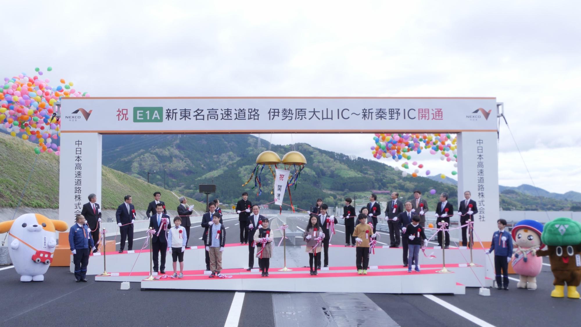 多数のカラフルな風船が舞う中で、地元の関係者や子どもたちが並んでテープカットを行なっている開通式の記念写真