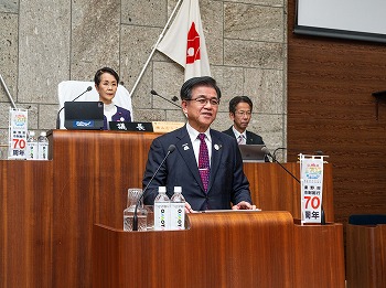 スーツ姿の高橋市長が議場の演壇で発言している様子の写真