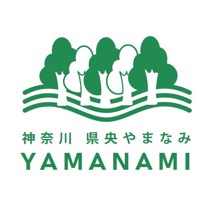 白い背景の上部に、濃い緑色で複数の木々が並ぶデザインが施され、その下には「神奈川県央やまなみ」「YAMANAMI」の文字が緑色のゴシック体で書かれたロゴマークのイラスト