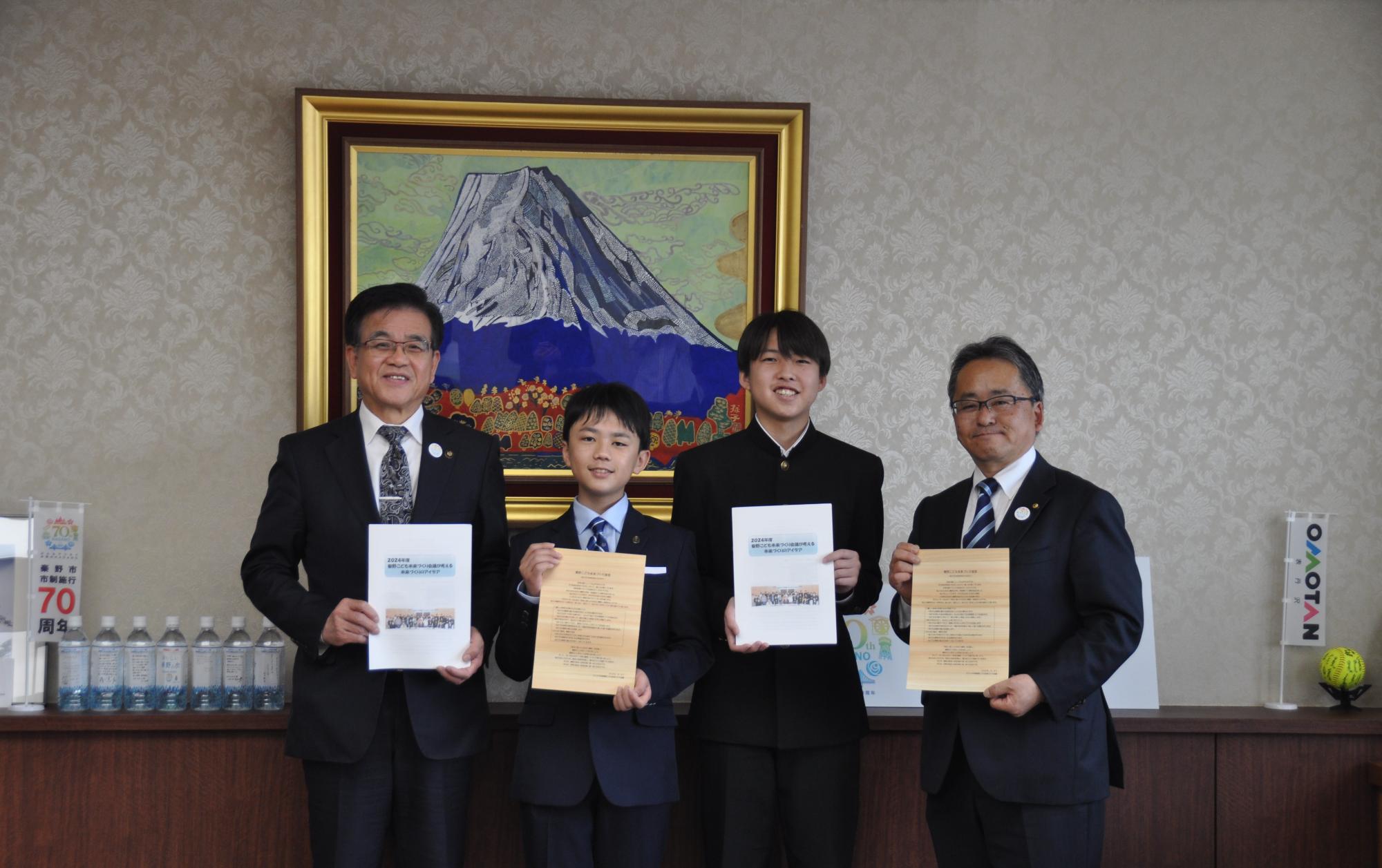 立派な富士山の絵画が飾られた室内で、左からスーツ姿の中年男性、学生服を着た少年、学ランを着た少年、スーツ姿の中年男性の計4人が並んでおり、それぞれが表彰状のような紙や書類を持ってカメラに向かって微笑んでいる記念写真