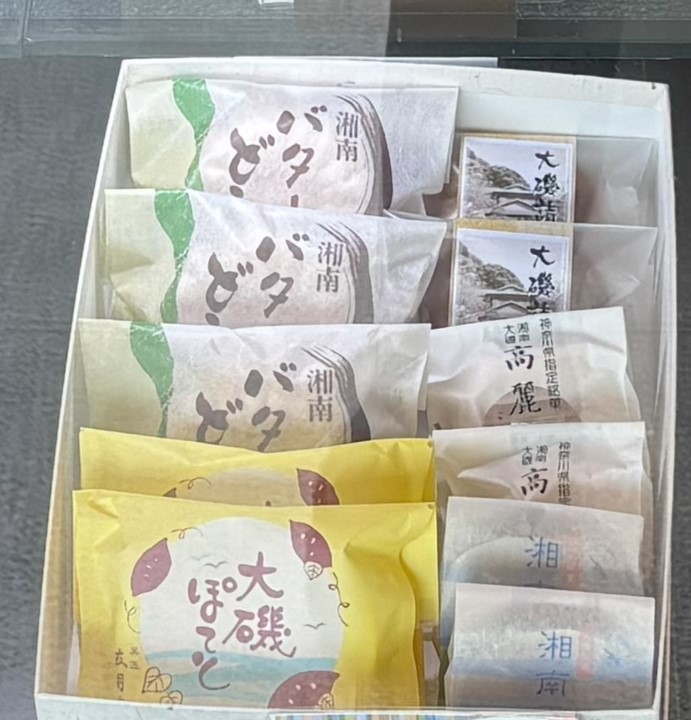 四つに区切られた白い箱の中に、上部には「湘南どらやき」と印字された和紙風の包みのどら焼きが三つ並び、右側には「大磯」の文字と風景写真がデザインされた箱入り菓子や、「湘南高麗」と書かれた包装紙の菓子、そして下段には黄色いパッケージの「大磯ぽてと」や「湘南」の文字が入った青い包装の羊羹のような菓子が詰められたお菓子の詰め合わせの写真