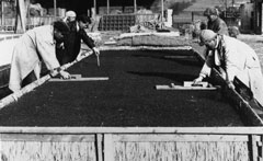 複数人が分担して落ち葉の上に土をまいている様子を写した古いモノクロ写真