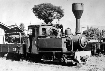 運転台の上に大きな煙突を装備した蒸気機関車が、無蓋貨車を連結して停車している様子の白黒写真