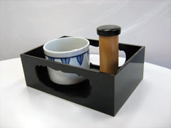白地に青い模様の入った湯呑みのような容器と、こげ茶色の筒状のものが黒い木製の運び盆に収められている様子の写真
