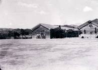 校庭の先に2棟の木造の校舎が建っている北中学校のモノクロ写真