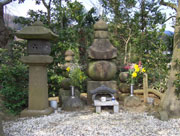 白い小石が敷き詰められた場所に、石灯籠や複数の石塔が並び、花や香炉が供えられた御首塚の写真
