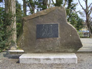 白い石の台座に乗った不揃いな形の大きな石に、文字が彫られた黒い石板が埋め込まれた石碑の写真