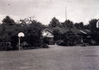 木々に囲まれた中に平屋の建物が建っている大根小学校のモノクロ写真