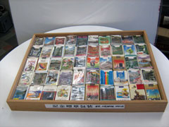 木の浅い箱の中に、日本の風景や名所などが描かれた観光煙草パッケージの箱が数十個、整然と並べられている写真