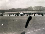 山並みを背景に建つ校舎を校庭から撮影した大根中学校のモノクロ写真