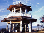 六角形をした二層の展望台が、夕焼けのような空の下で遠くに山々を望む高台に建っている弘法山公園の写真