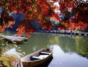 水面にボートが浮かび、対岸の木々や紅葉した木の枝が鮮やかに写り込んでいる、震生湖の写真