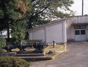 コンクリートの建物の前に、樹木に囲まれた、古い配水装置が置かれている曽屋配水場の写真