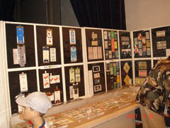 多くの古いタバコのパッケージやレトロなデザインの喫煙関連グッズが、白い枠の黒いパネルに整然と展示され、手前の机にも多数の展示品が並べられている展示会の様子の写真