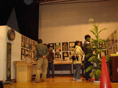 広々とした展示会場の壁に様々なパネルが掲げられており、数人の来場者がそれらを鑑賞している様子の写真