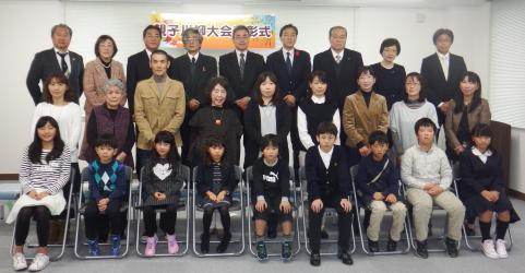 「親子川柳大会表彰式」と書かれた横断幕の下で、27人の関係者と親子が3列に並び記念撮影をしている集合写真