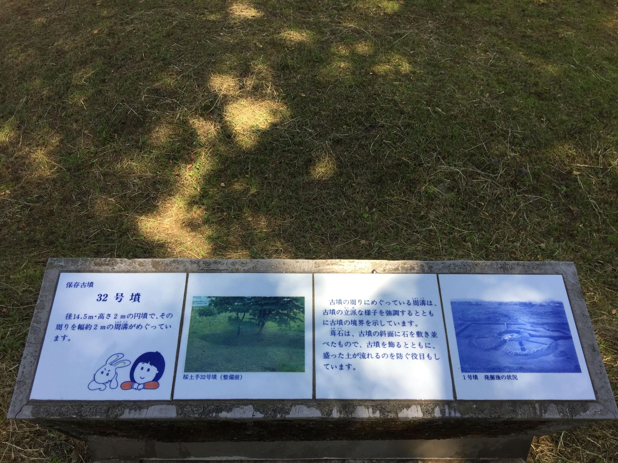 木陰に設置された、古墳の空撮写真や説明書きなど4枚の四角いパネルからなる、32号墳の案内板の写真