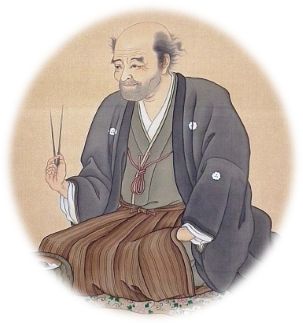 紋付き袴姿で火ばさみを右手に持って座っている安居院庄七の肖像画