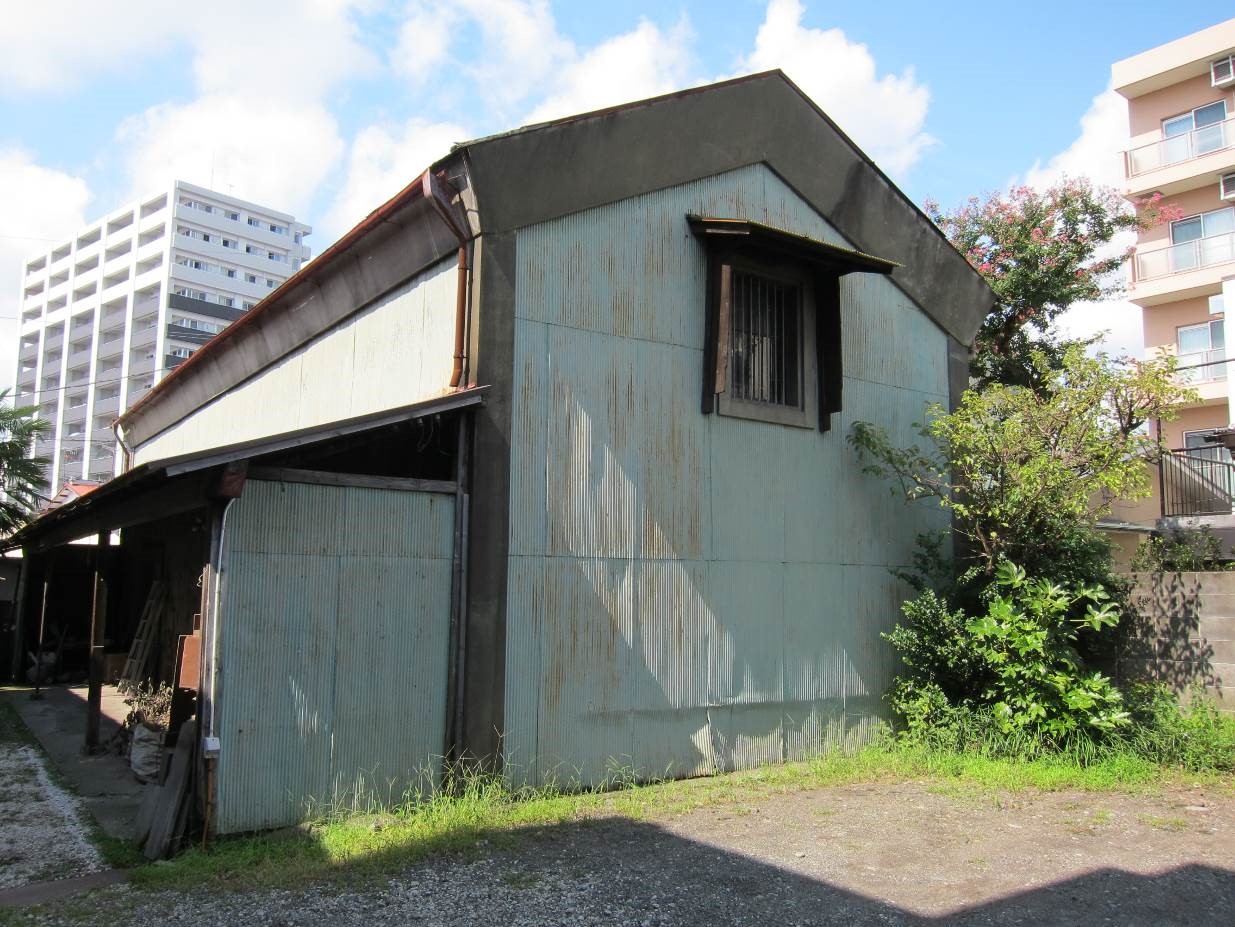 青く錆びた波板が外壁に使われた、年季の入った倉庫のような平屋の建物を写した写真