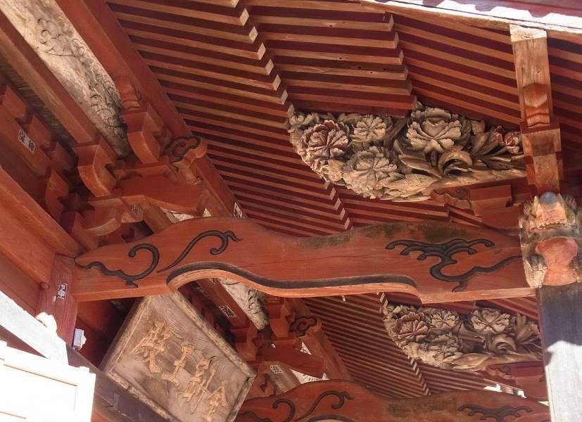 朱色に塗られた屋根の下部分に花などの彫刻が施された大日堂向拝海老虹牡丹彫刻の写真