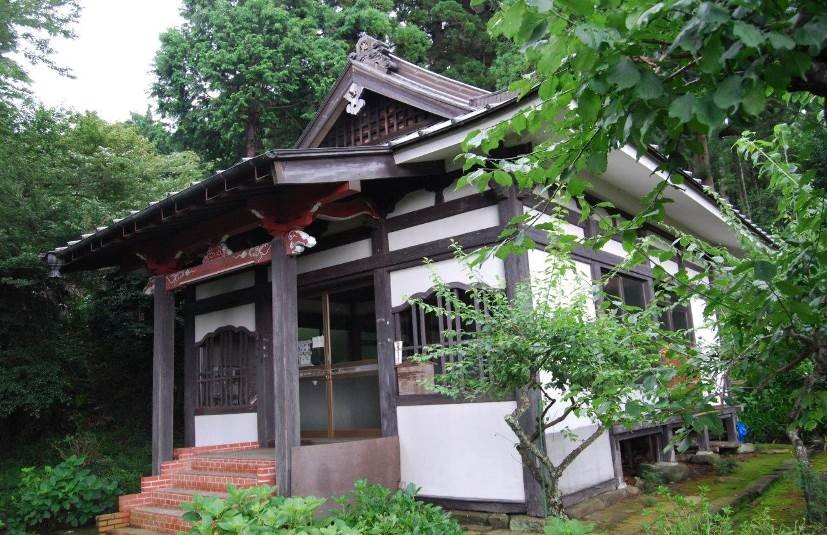 緑の木々や植栽に囲まれて建つ、白い壁と茶色の柱のコントラストが特徴的な不動堂の外観写真