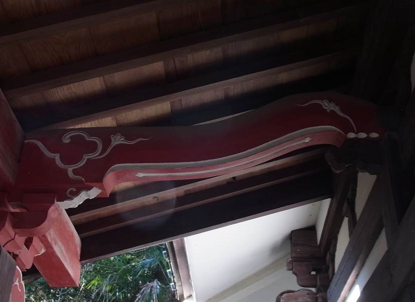屋根の下部分にある、赤く塗られ、白い線で模様が描かれた不動堂向拝海老虹梁の写真