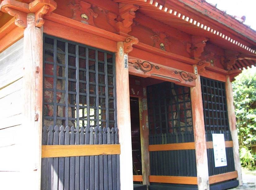 鮮やかな朱色の柱や屋根の建物の左右が黒い格子で仕切られ、中に1体ずつ仁王像が安置されている仁王門の軒下の写真