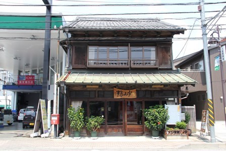 濃い茶色の木造の2階建ての建物で1階の正面には「ますや」という暖簾と鉢植えが置かれた店先の写真