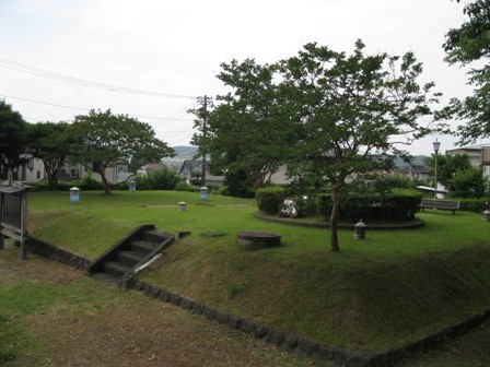 小さな灯籠やベンチが設置された、なだらかな芝生の丘が広がる公園を写した写真